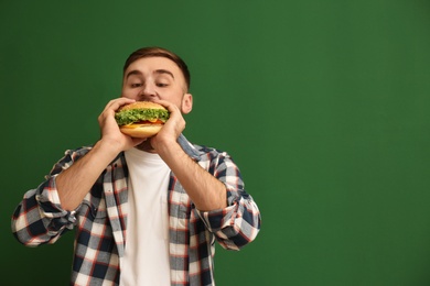 Young man eating tasty burger on color background. Space for text