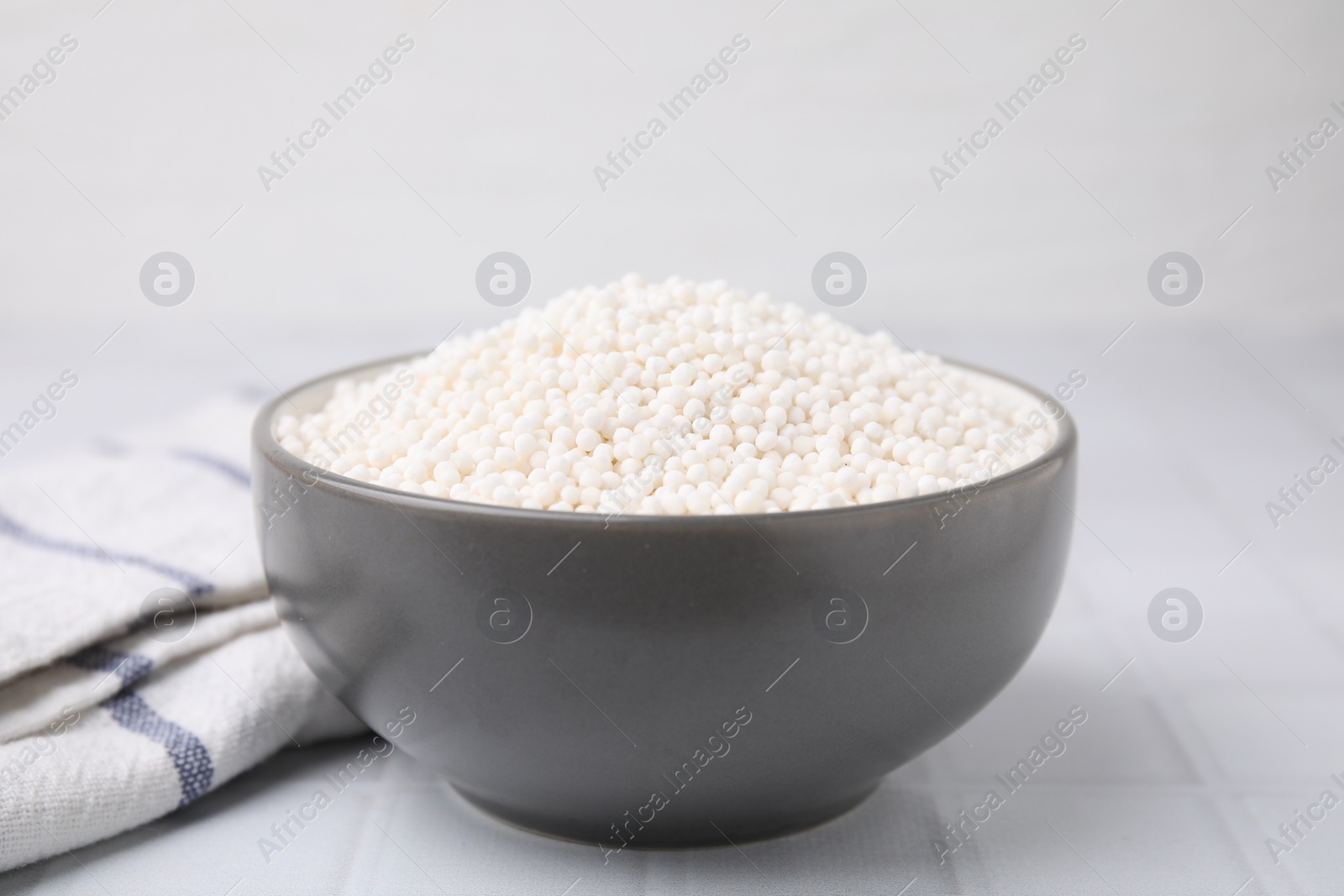 Photo of Tapioca pearls in bowl and towel on white tiled table