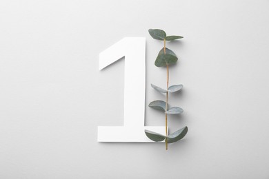 Photo of Paper number 1 and eucalyptus branch on light grey background, top view