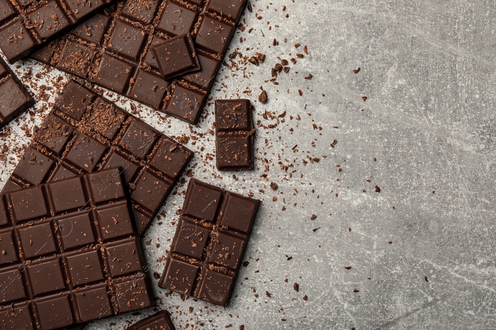 Photo of Pieces and shavings of tasty chocolate bars on light grey table, flat lay. Space for text