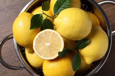 Fresh lemons and green leaves in colander on wooden table, top view