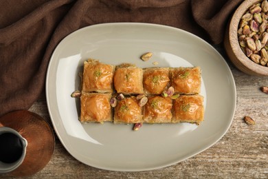 Delicious baklava with pistachios and hot coffee on wooden table, flat lay