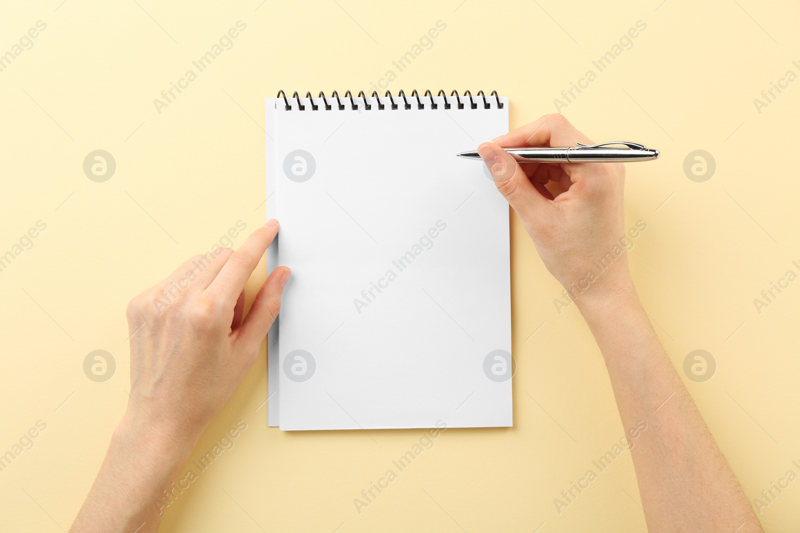 Photo of Woman writing in notebook on beige background, top view