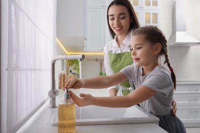 Mother and daughter washing hands with liquid soap in kitchen