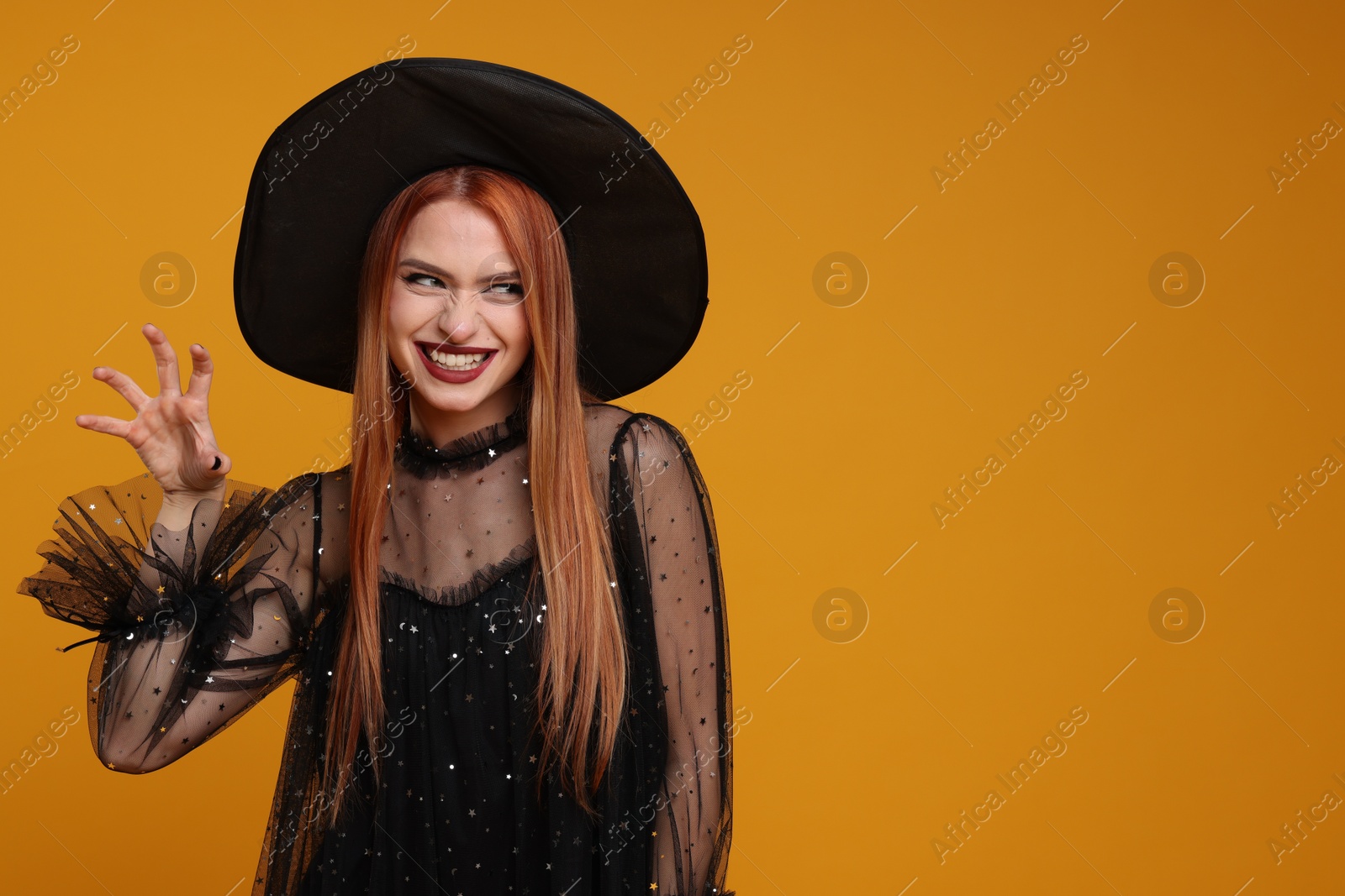 Photo of Happy young woman in scary witch costume on orange background, space for text. Halloween celebration