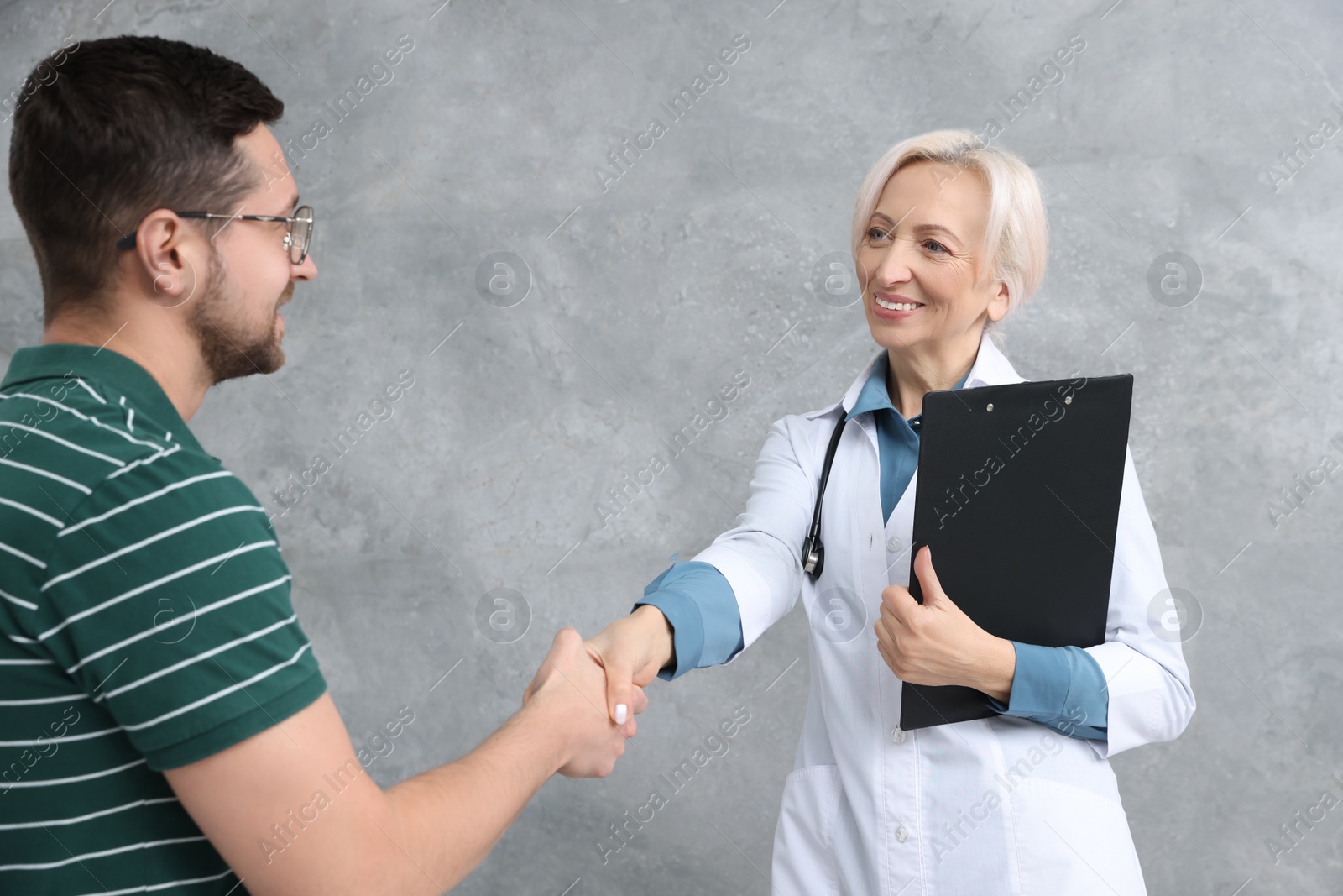 Photo of Doctor shaking hands with patient after consultation near grey wall