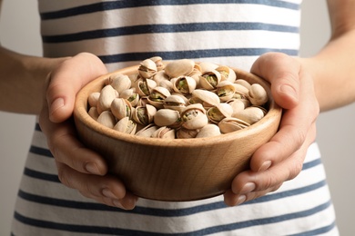Photo of Woman holding bowl with pistachio nuts on light background, closeup