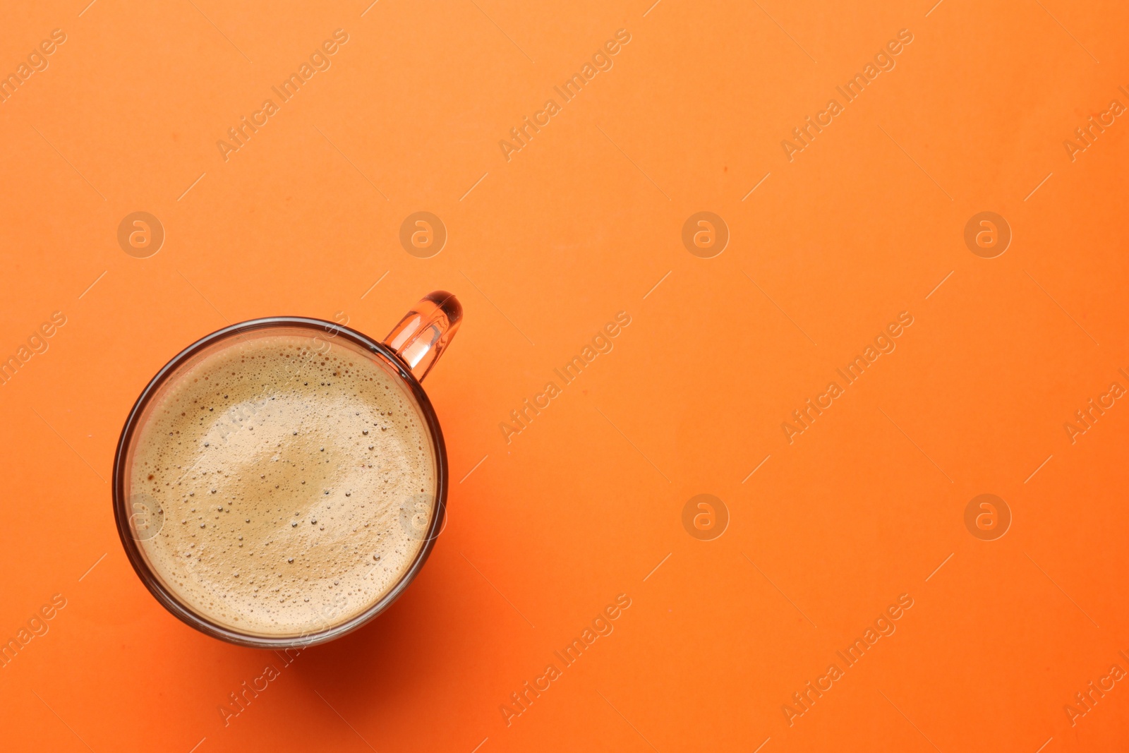 Photo of Fresh coffee in cup on orange background, top view. Space for text