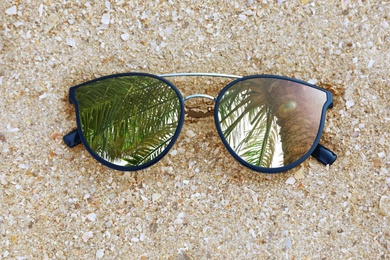 Green palm leaves reflecting in sunglasses on sandy beach, top view