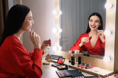 Photo of Beautiful woman applying makeup near mirror in room