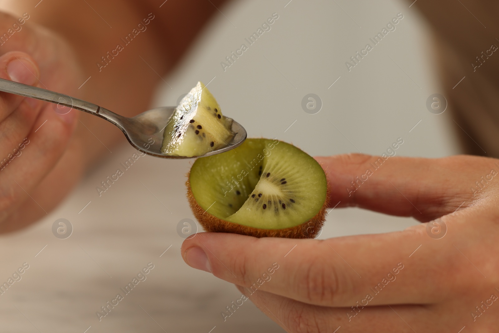 Photo of Man eating kiwi with spoon on blurred background, closeup