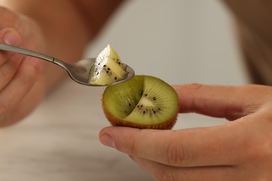 Man eating kiwi with spoon on blurred background, closeup