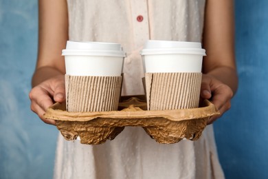 Photo of Woman holding cardboard holder with takeaway paper coffee cups on light blue background, closeup