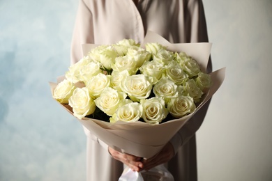 Woman holding luxury bouquet of fresh roses on light blue background, closeup
