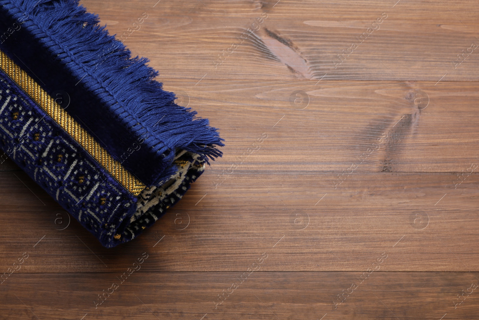 Photo of Muslim prayer rug on wooden table, above view. Space for text