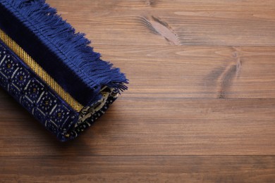 Photo of Muslim prayer rug on wooden table, above view. Space for text