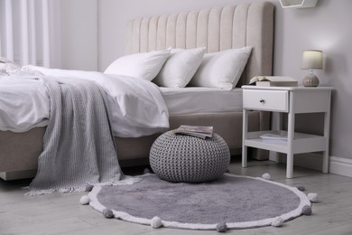 Stylish bedroom interior with knitted pouf and furniture