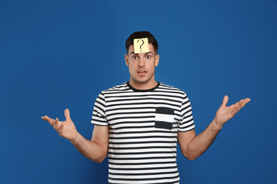 Emotional man with question mark sticker on forehead against blue background