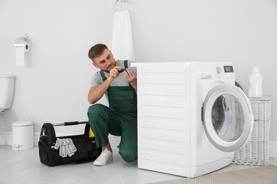 Young plumber fixing washing machine in bathroom