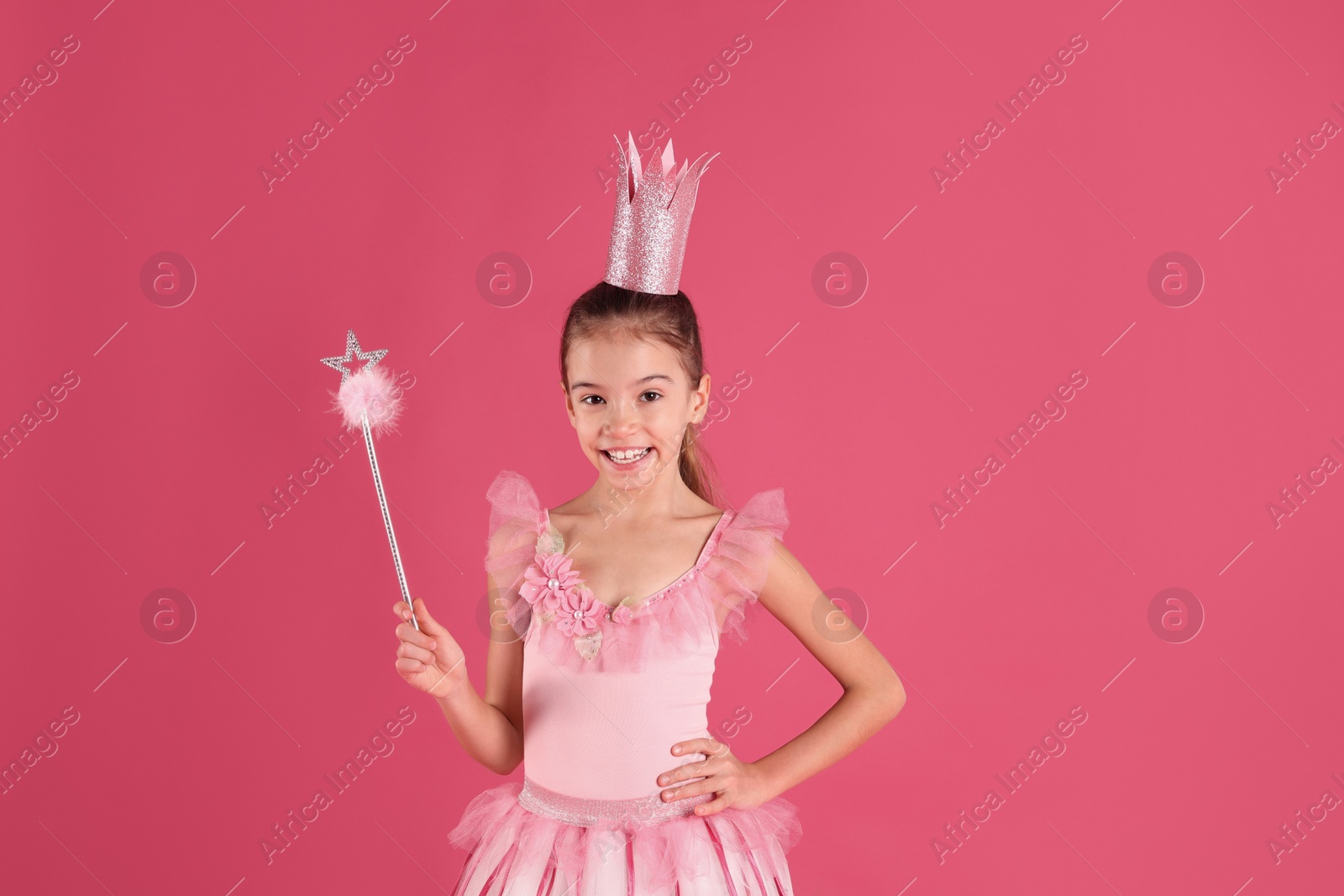 Photo of Cute girl in fairy dress with crown and magic wand on pink background. Little princess