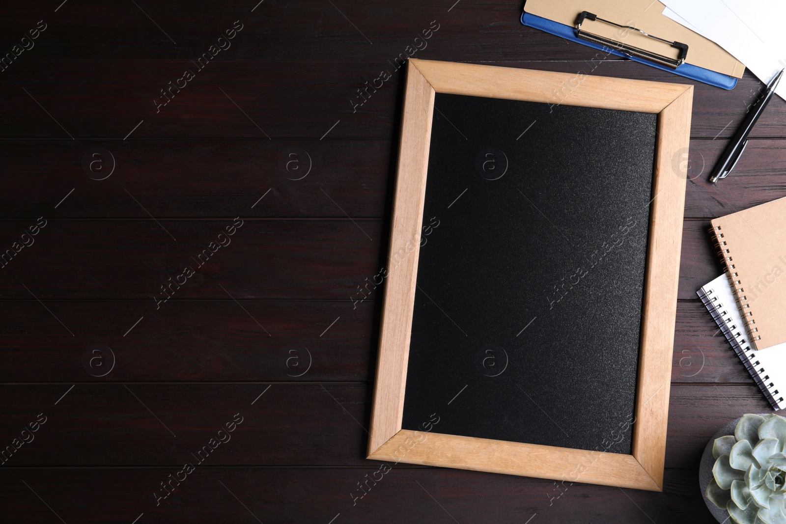 Photo of Clean small chalkboard, plant and stationery on wooden table, flat lay. Space for text