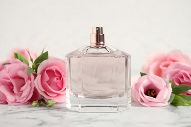 Photo of Bottle of perfume and beautiful flowers on white marble table