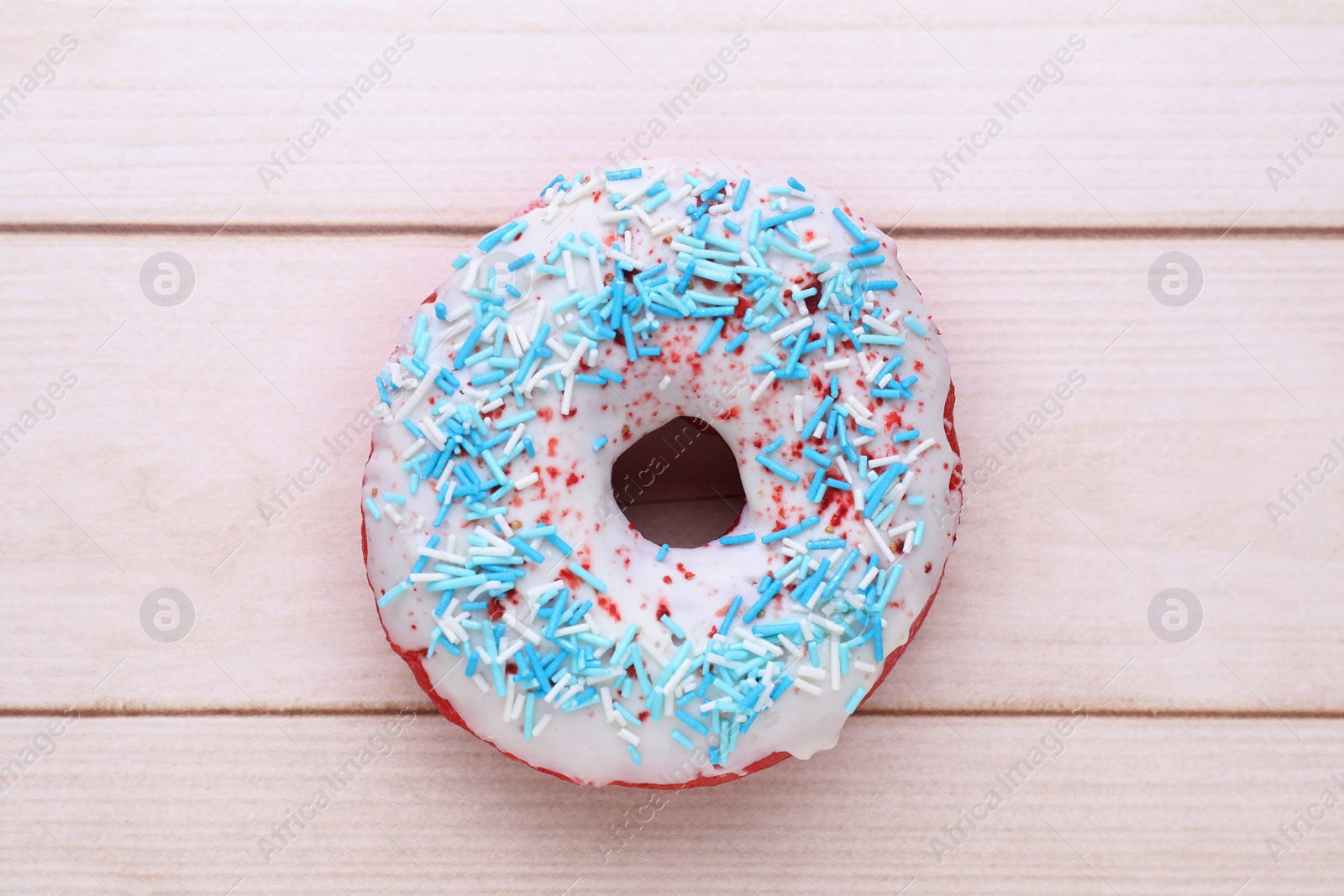 Photo of Glazed donut decorated with sprinkles on white wooden table, top view. Tasty confectionery