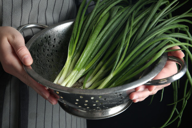 Photo of Woman holding colander with green spring onions, closeup