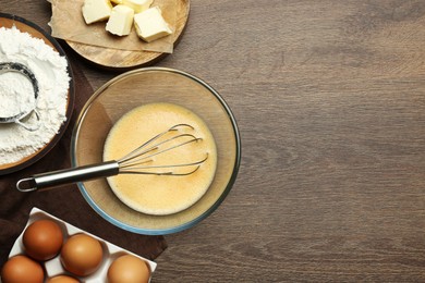 Photo of Beaten eggs, whisk and ingredients on wooden table, flat lay. Space for text