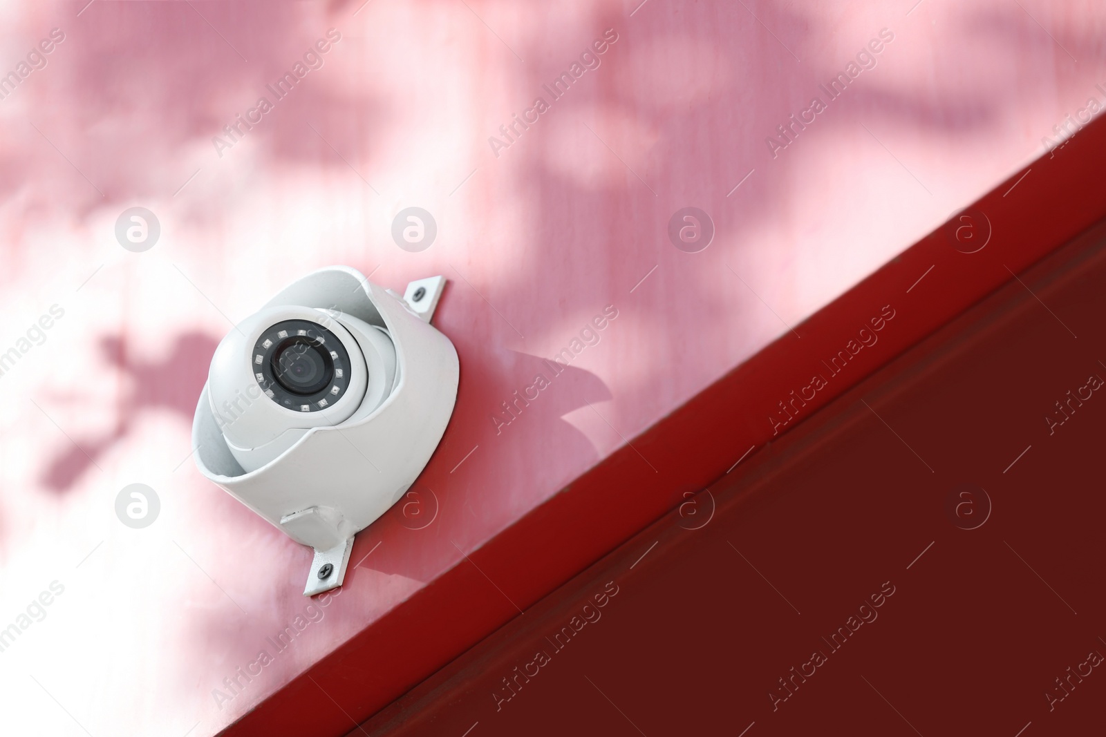 Photo of Modern CCTV security camera on red building wall outdoors. Space for text