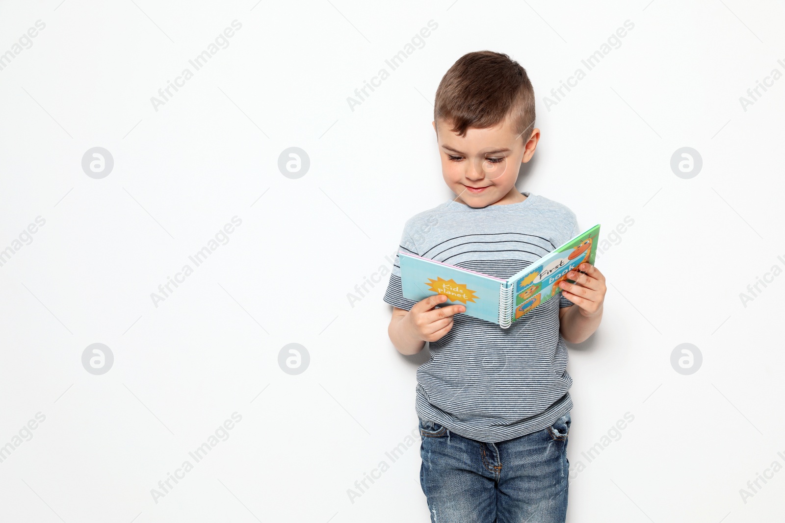 Photo of Cute little boy reading book on white background, space for text