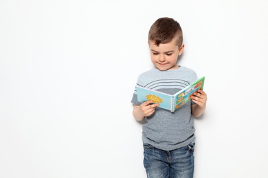 Cute little boy reading book on white background, space for text