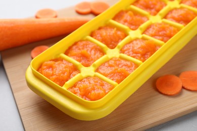 Carrot puree in ice cube tray on wooden board, closeup. Ready for freezing