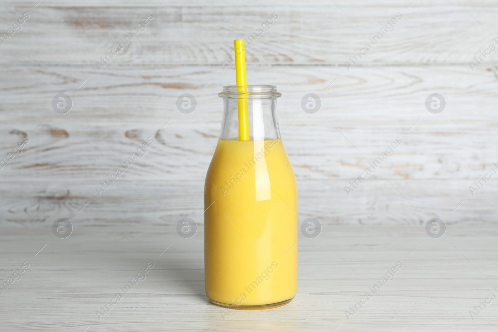 Photo of Bottle of tasty smoothie with straw on white wooden table