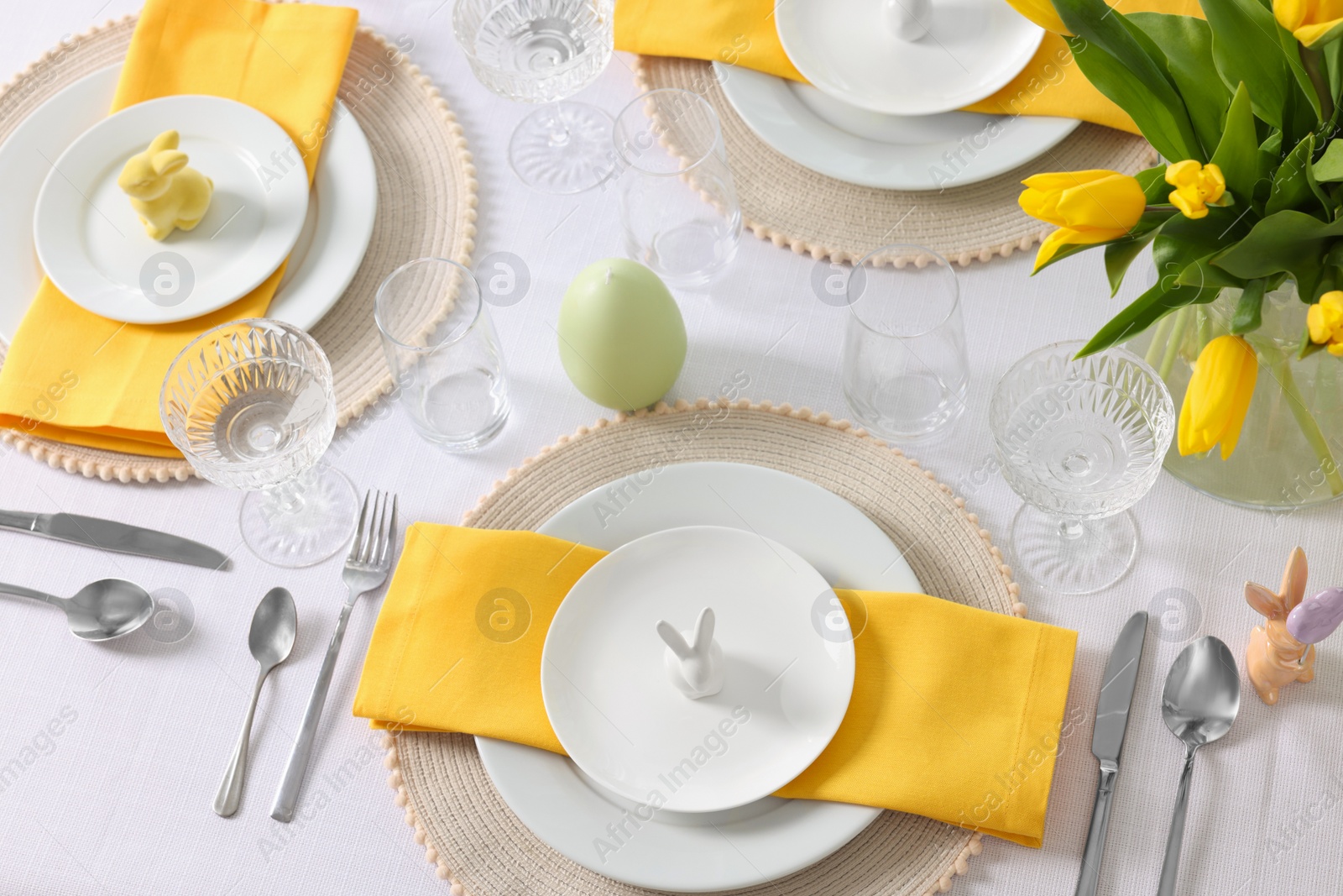 Photo of Festive table setting with glasses, plates and vase of tulips. Easter celebration