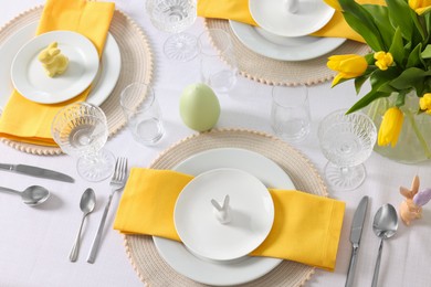 Festive table setting with glasses, plates and vase of tulips. Easter celebration