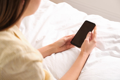 Young woman using modern smartphone on bed at home, closeup