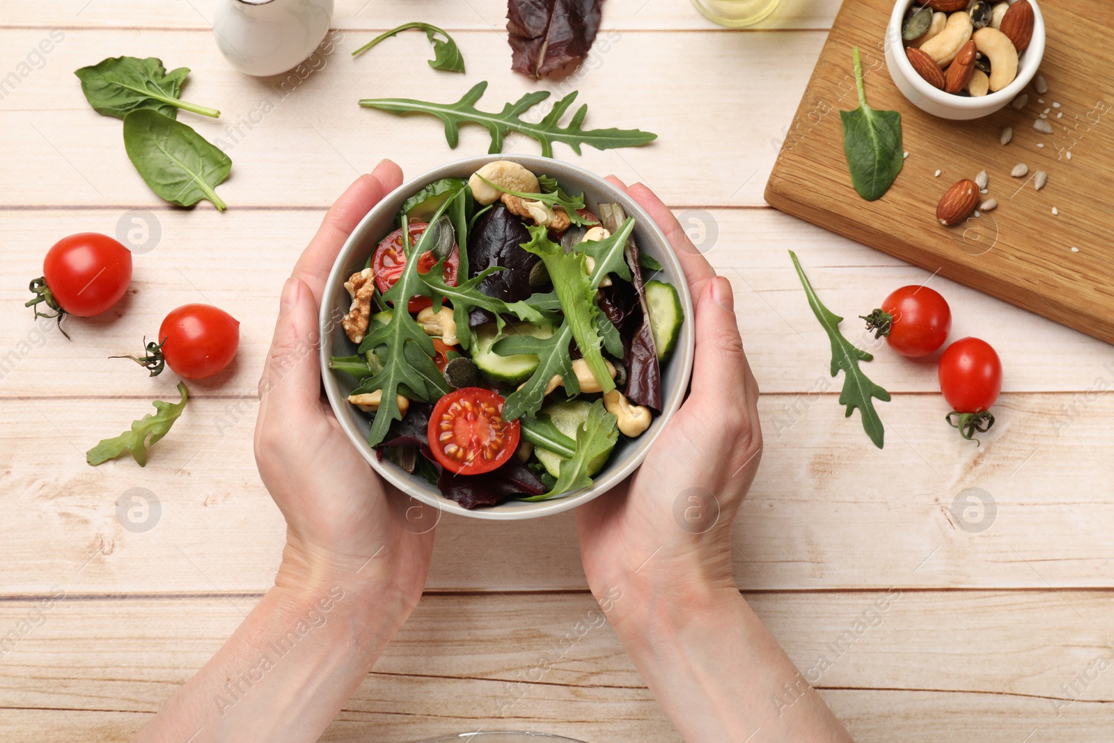 Photo of Woman with tasty fresh vegetarian salad at light wooden table, top view