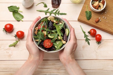 Woman with tasty fresh vegetarian salad at light wooden table, top view