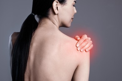 Woman suffering from shoulder pain on grey background, closeup