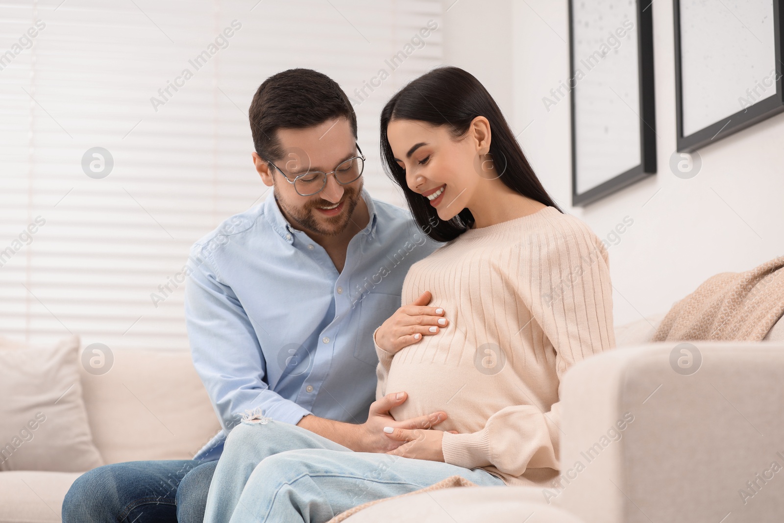 Photo of Happy pregnant woman spending time with her husband on sofa at home