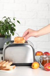 Photo of Woman taking off roasted bread from toaster, closeup