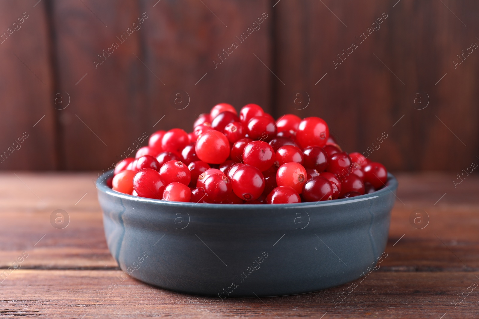 Photo of Fresh ripe cranberries in bowl on wooden table, closeup