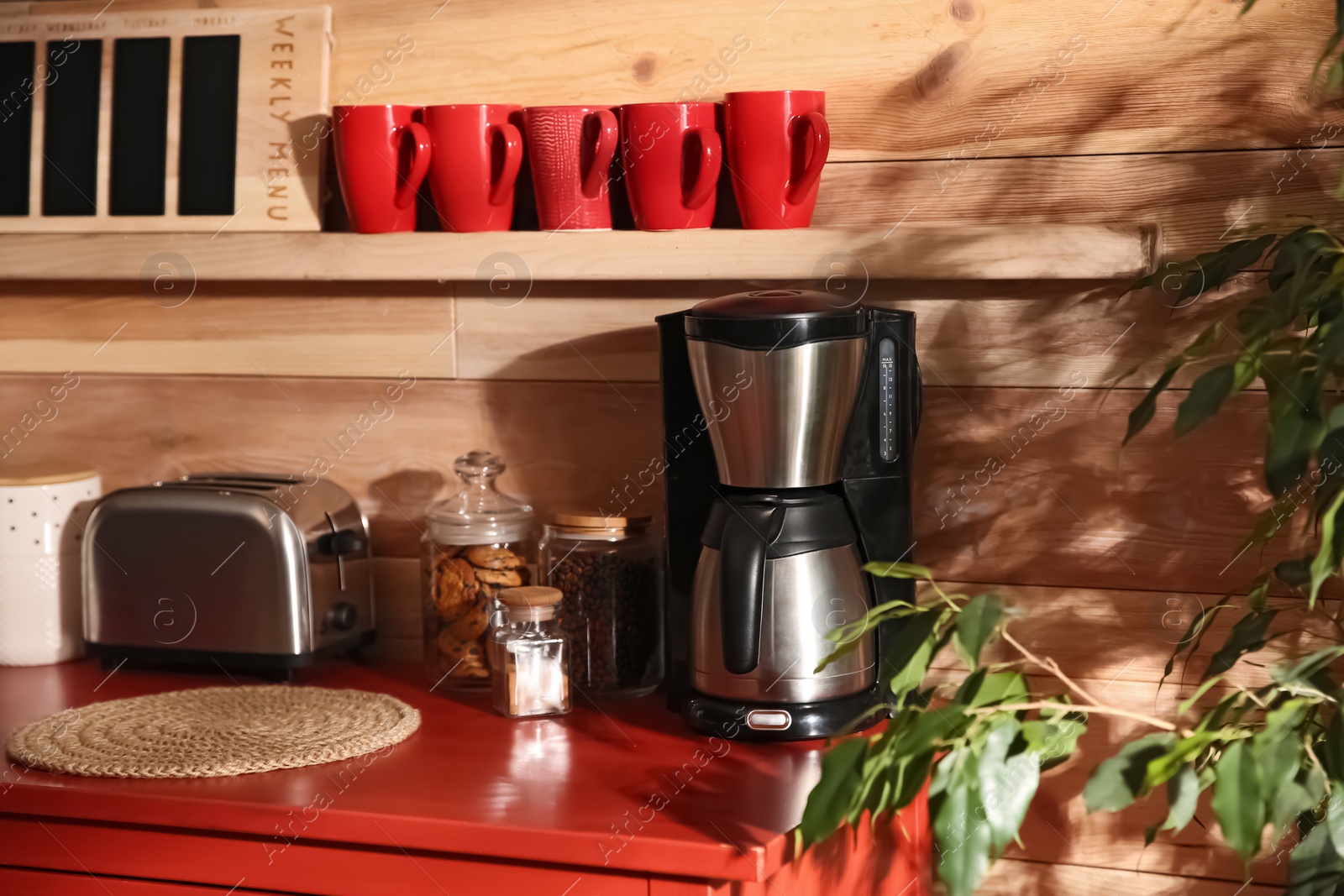 Photo of Modern coffeemaker and toaster on red table near wooden wall