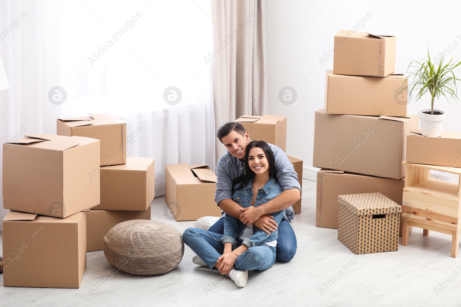 Photo of Happy couple in room with cardboard boxes on moving day