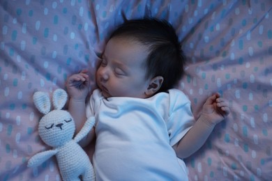 Photo of Cute newborn baby sleeping with toy bunny in crib at night, top view