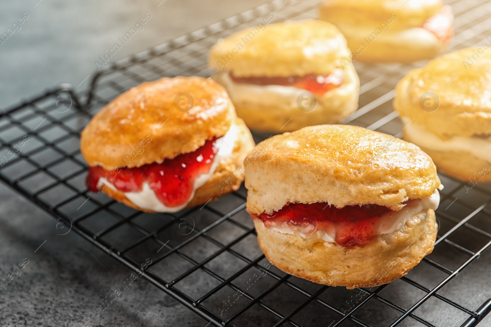 Photo of Tasty scones with clotted cream and jam on cooling rack, closeup