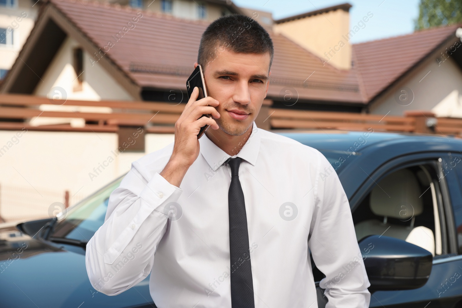 Photo of Attractive young man talking on phone near luxury car outdoors