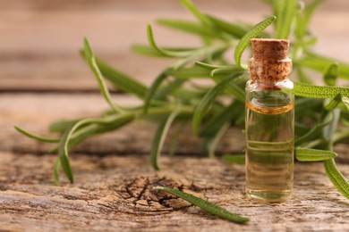 Aromatic essential oil in bottle and rosemary on wooden table, closeup. Space for text