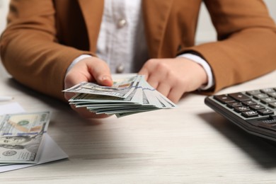 Photo of Money exchange. Woman holding dollar banknotes at white wooden table, closeup